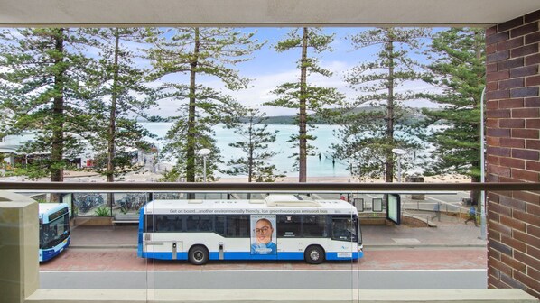 En buss med en affisch på sidan, parkerad framför en byggnad med utsikt över träd och vatten.