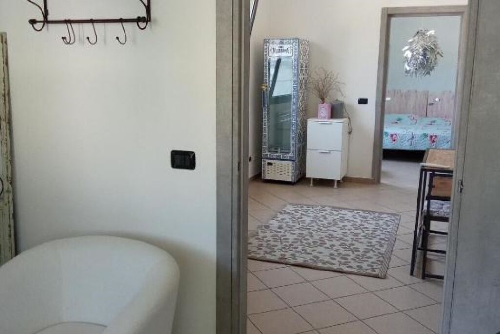 Una habitación con una cama, un armario pequeño blanco, un espejo y una puerta que da a otra habitación.