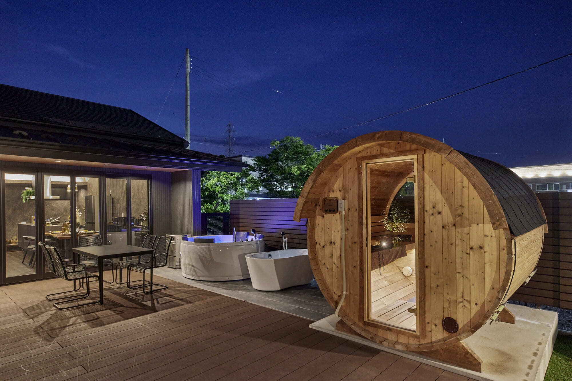 Una cabaña de madera con puerta circular, un jacuzzi y un comedor con sillas y una mesa.