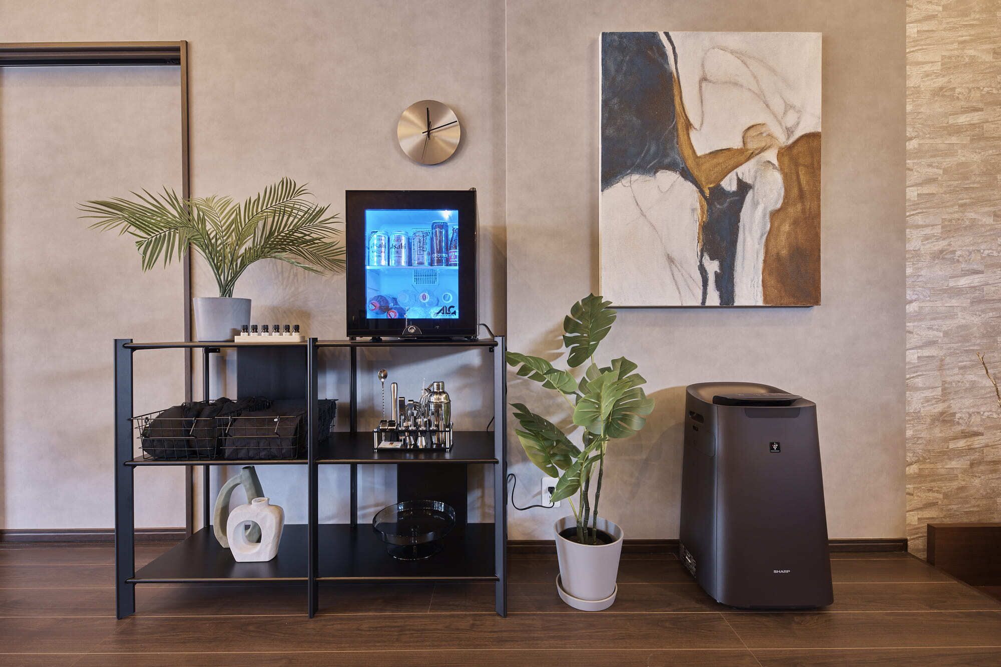 A modern living room with a flat-screen TV, a clock, a painting, a potted plant, a speaker, and a shelf with various items.