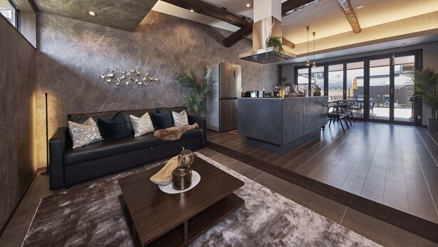 Una sala moderna con un sofá oscuro, una mesa de centro y una zona de cocina con barra.