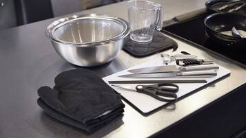 Una encimera de cocina con un bol de acero inoxidable, una jarra de vidrio, un cuchillo, tijeras y guantes de horno negros.
