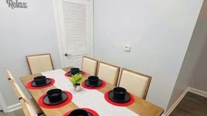 Una mesa de comedor con seis sillas, un florero con planta y un mantel individual rojo y blanco.