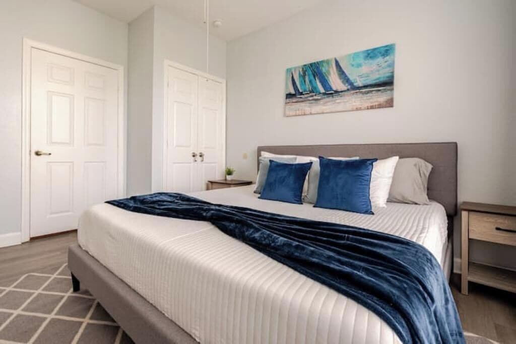 Ein Schlafzimmer mit einem Bett, einem Nachttisch, einem Bild an der Wand und zwei Türen.