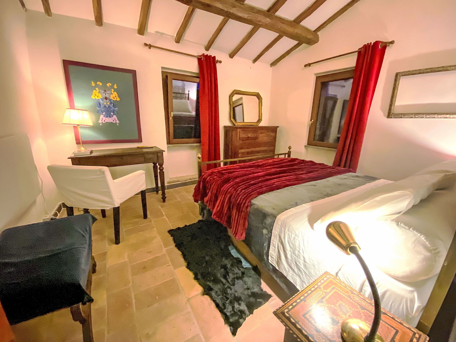 Ein Schlafzimmer mit einem Bett, einem Schreibtisch, einem Stuhl, einer Kommode und einem Fenster mit roten Vorhängen.