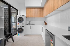 Une cuisine compacte équipée d’un lave-linge et d’un sèche-linge intégrés, d’un évier et d’un lave-vaisselle.
