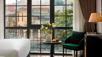 Una habitación con un ventanal grande, una mesa redonda con un florero y una silla verde, además de una lámpara.