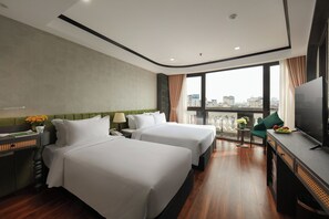 A hotel room with two beds, a TV, a small table with fruit, and a balcony with a view of the city. - Hanoi Plaza Suite Hotel & Spa (Hanoi)
