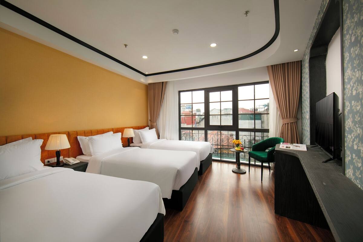 A hotel room with two beds, a desk, a TV, and a balcony with a view.