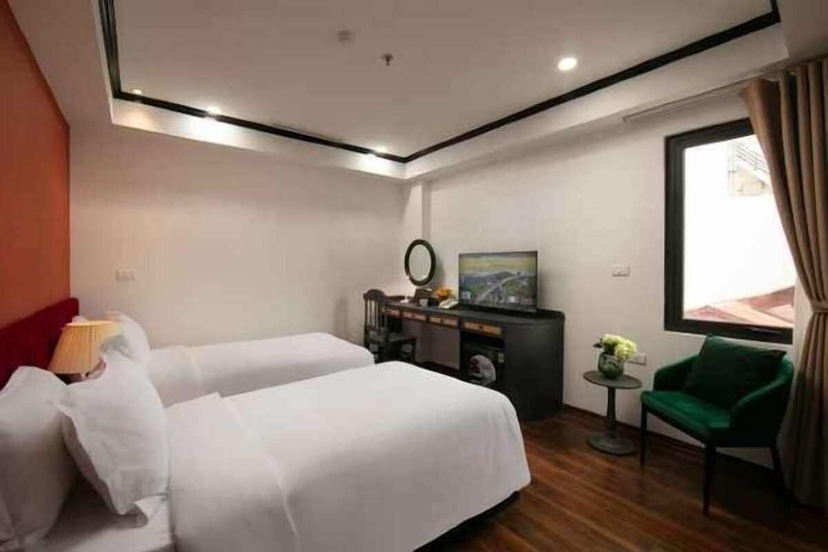 Habitación de hotel con dos camas, un escritorio con una silla, una mesita con una planta y un ventanal grande.