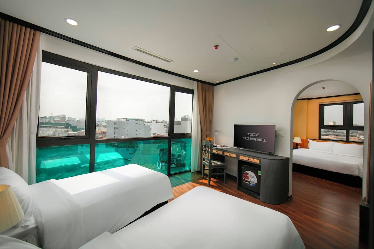 A hotel room with two beds, a TV, a desk, and a view of the city.