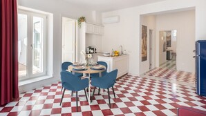 Una cocina moderna con armarios blancos, una zona de comedor con sillas azules y un suelo a cuadros.