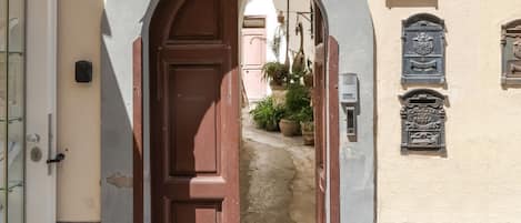 An arched doorway leading to a courtyard with potted plants and a sign indicating "Taure Charming Accommodation".