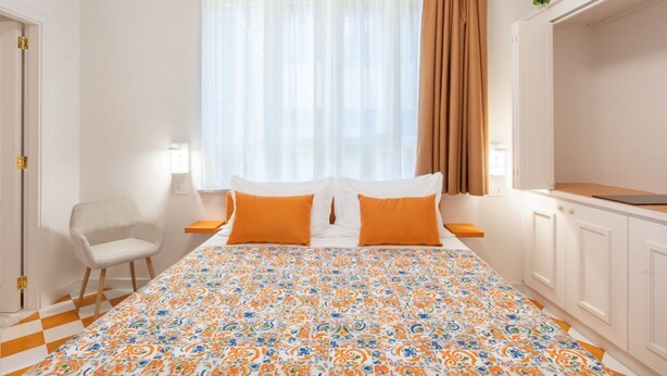 A bedroom with a bed, two pillows, a chair, a window with curtains, and a small plant on the window sill.