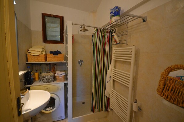 A bathroom with a shower, a sink, a mirror, and a shelf with toiletries. - Peaceful Ligurian Hill Stay (Stellanello)