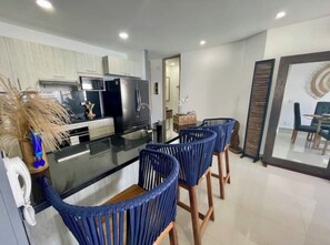 A modern kitchen with a central island, bar stools, and a dining area with a view. - Panoramic High-Rise Oceanview Condo in Bocagrande (Bocagrande)
