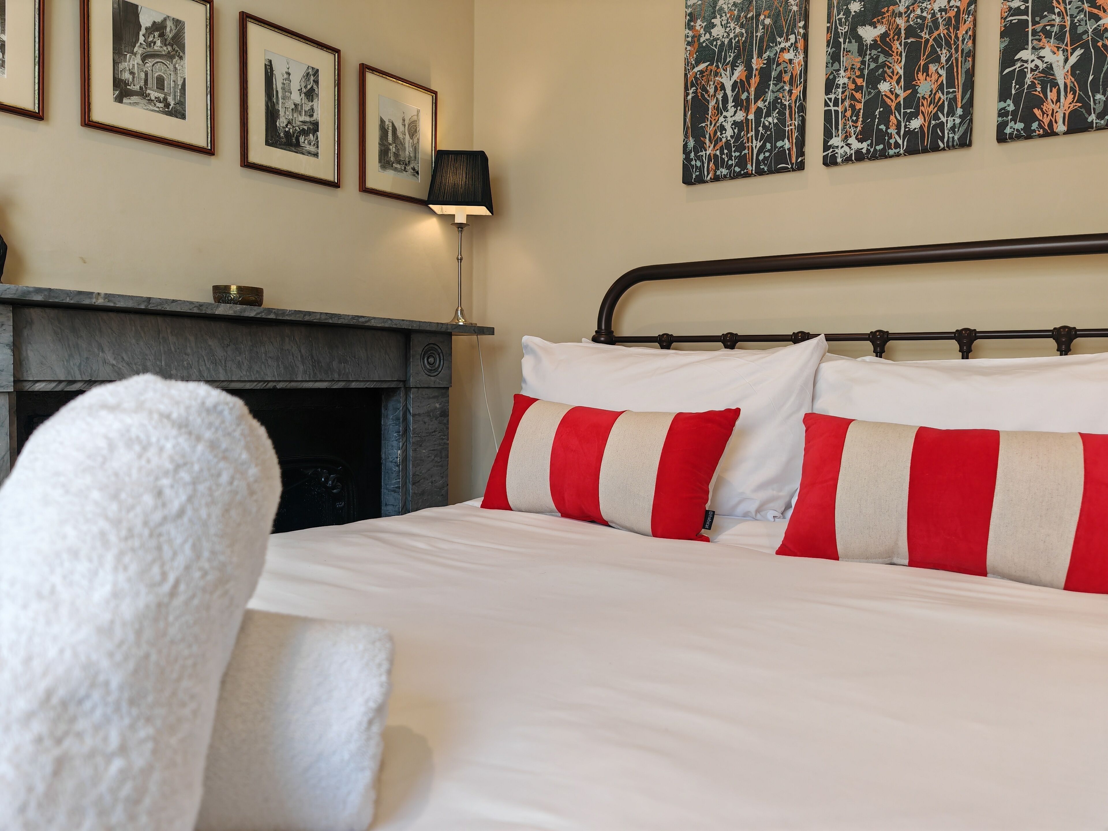 A hotel room with a bed, a fireplace, and framed pictures on the wall.