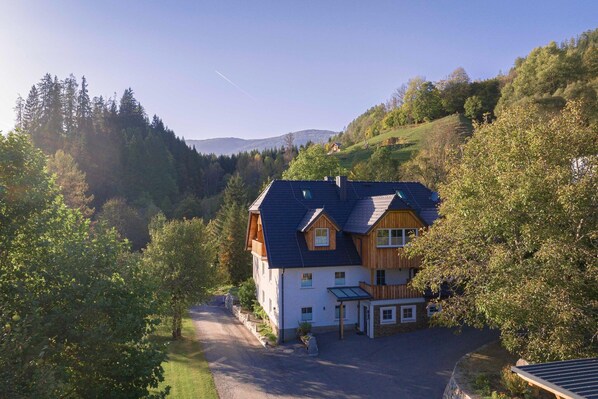 Una casa a due piani con tetto spiovente, immersa nel verde e circondata da alberi.