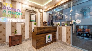 A reception area with a wooden desk, a sign reading "treebo," and a glass wall with a view of the outside. - Treebo AK Residency (Rishikesh)