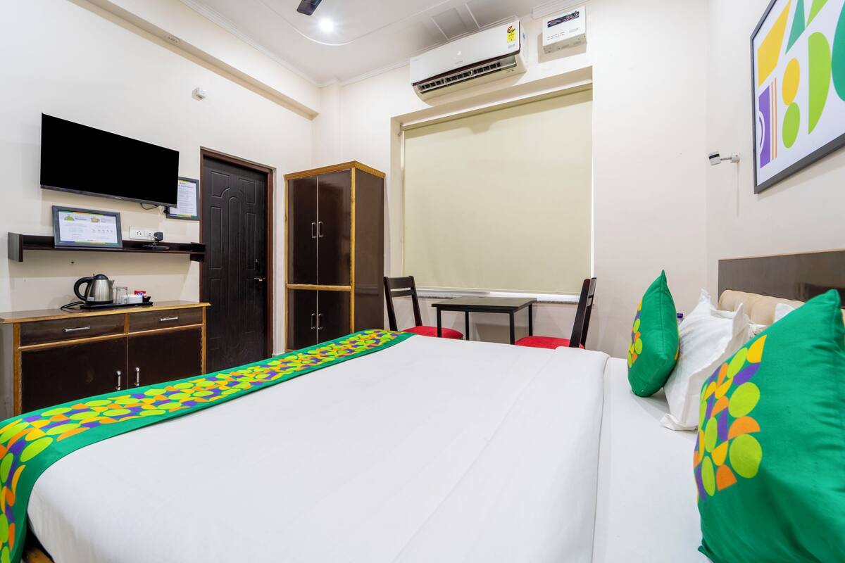 A hotel room with a bed, a desk, a chair, a wardrobe, a television, and an air conditioning unit.