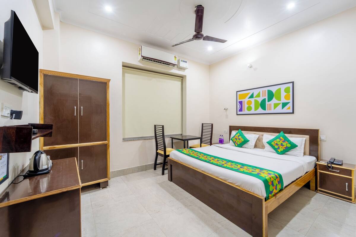 A hotel room with a bed, a desk, a chair, a wardrobe, a television, an air conditioning unit, and a ceiling fan.