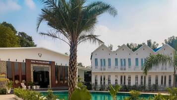 Ein Hotel mit Poolbereich, Palmen und einem Gebäude mit weißer Fassade und blauen Fenstern.