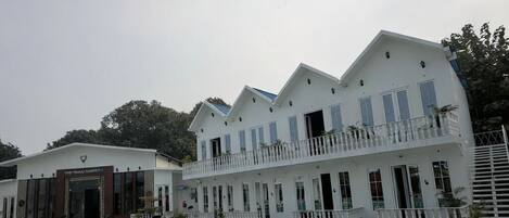 A hotel with a swimming pool, multiple balconies, and a white facade.