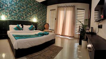A modern bedroom with a large bed, a nightstand, a mirror, a potted plant, and a TV on a shelf.