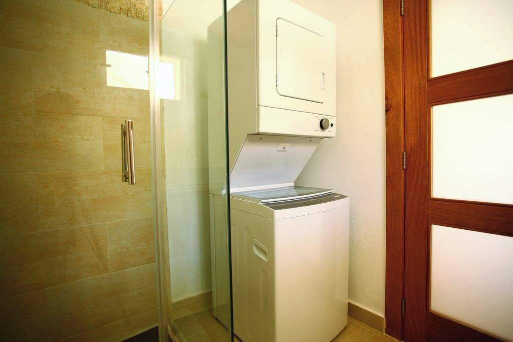 A compact laundry room with a washing machine and dryer, a glass shower enclosure, and a wooden door.
