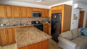 Cocina con gabinetes de madera, encimeras de granito, electrodomésticos de acero inoxidable y un sofá beige en la sala contigua.