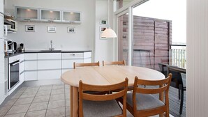 Une cuisine moderne avec des meubles blancs, une table à manger avec quatre chaises et un balcon agrémenté d’une clôture en bois.
