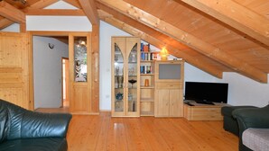 Une pièce mansardée chaleureuse avec des poutres apparentes, une télévision, une bibliothèque et un canapé en cuir.