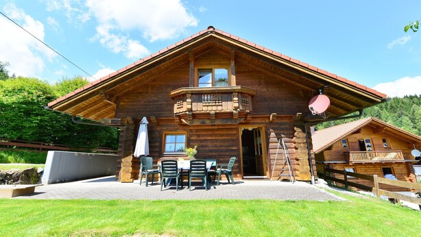 Un chalet en bois doté d’un balcon, d’une terrasse avec des meubles d’extérieur et offrant une vue sur les montagnes.