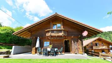 Eine Holzhütte mit Balkon, einer Terrasse und Sitzgelegenheiten im Freien, vor einer Bergkulisse.