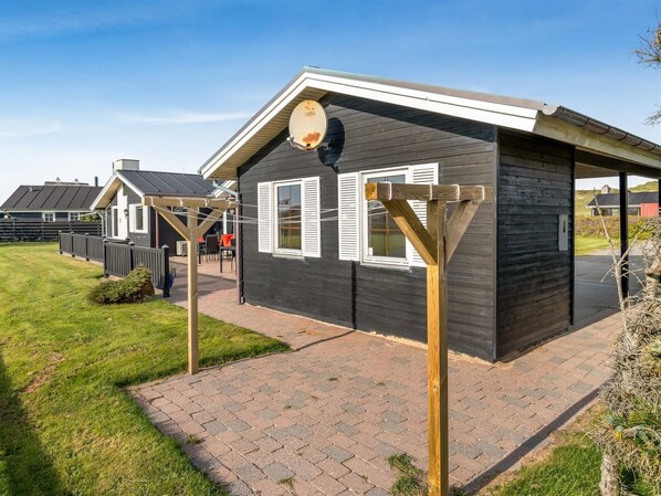 Een modern huis met een donkere gevel, een houten pergola en een verharde oprit.