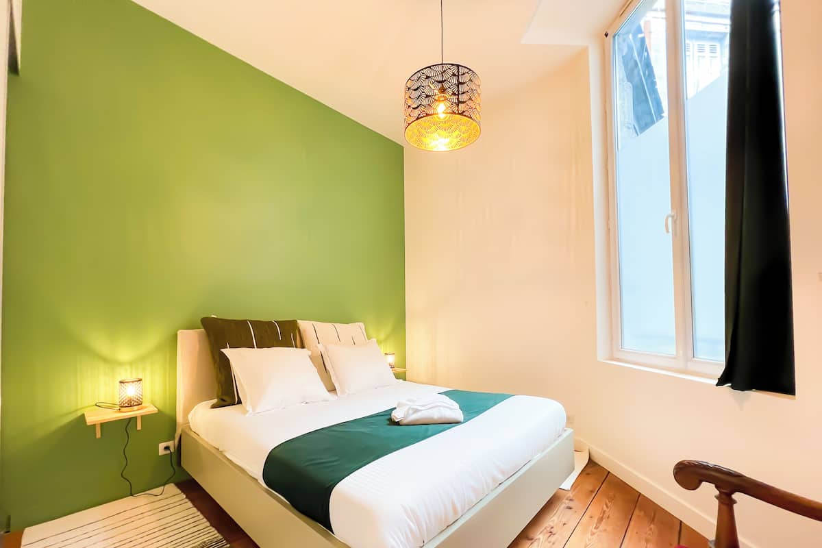 A bedroom with a bed, a nightstand, a lamp, and a window.