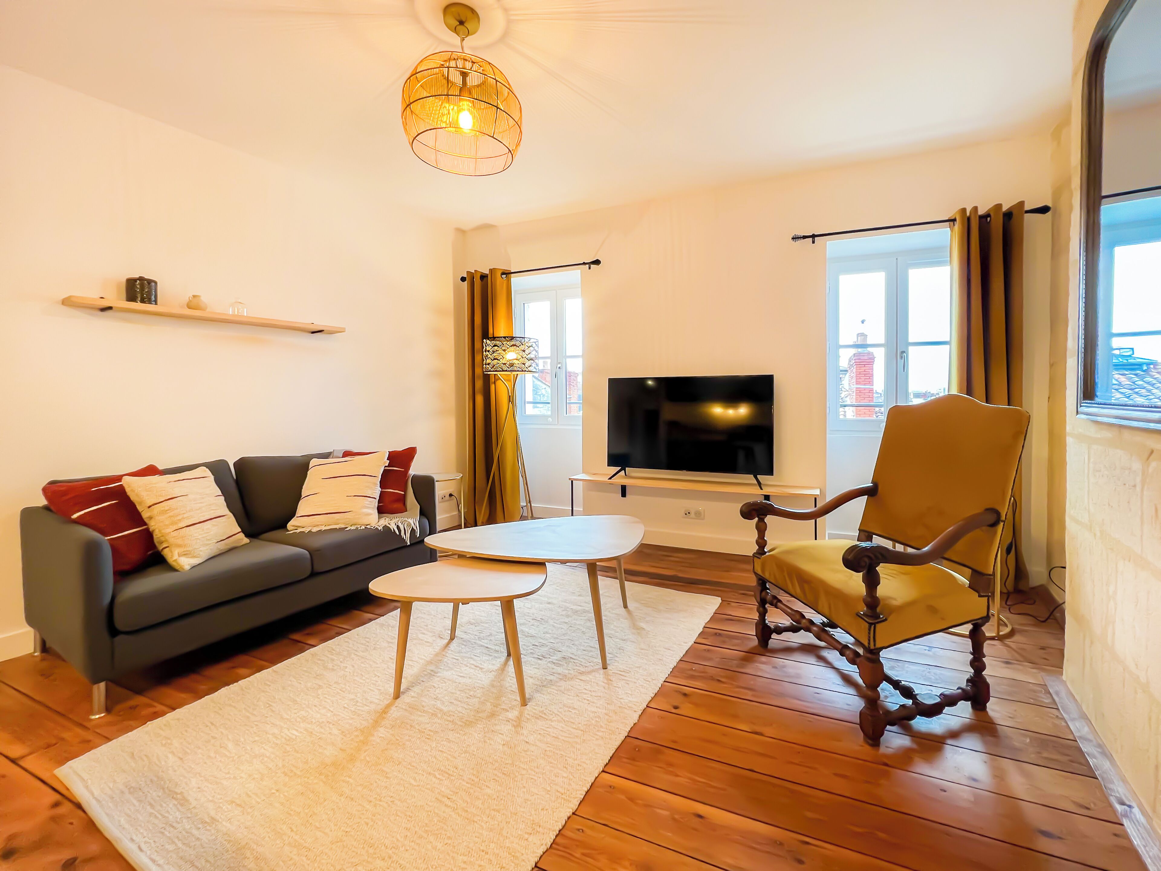 Un salon comprenant un canapé, une table basse, un fauteuil, un téléviseur et une fenêtre avec des rideaux.