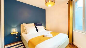 A neatly made bed with white and yellow bedding, a bedside lamp, and a window with curtains.