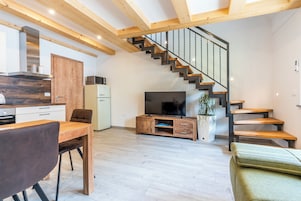 Una sala de estar moderna con una escalera de madera, un comedor y una cocina.