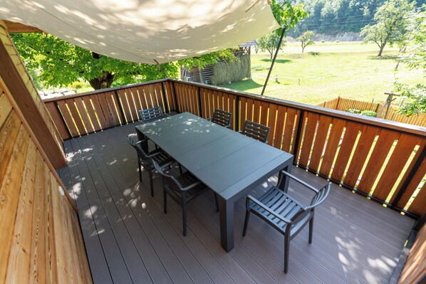 Een overdekt terras met een tafel en stoelen, omringd door een houten hek, met uitzicht op een gazon.
