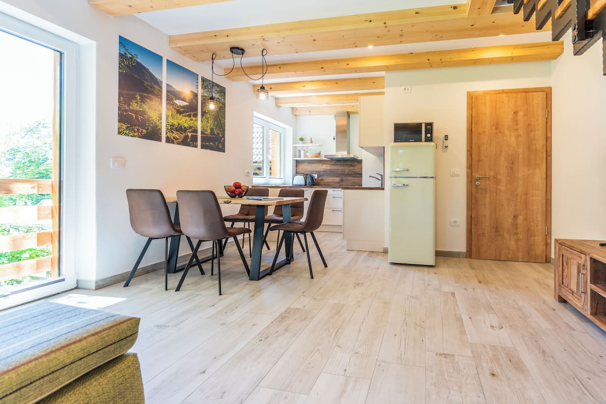 A modern kitchen with wooden beams, a dining area with a table and chairs, and a view of the outdoors.
