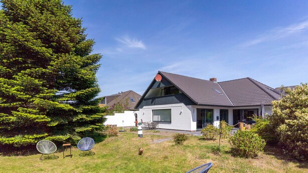 A modern house with a sloped roof, a large tree, and a grassy yard with outdoor furniture.