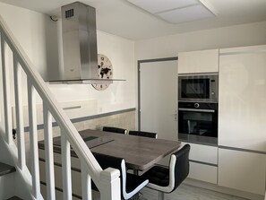 Ett modernt kök med en matplats, inklusive en trappa, en världsklocka och inbyggda vitvaror.