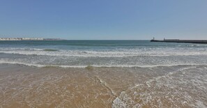 A beach with waves, a pier, and a lighthouse in the distance. - Appartement vue CHENAL I Les Sables I parking (Les Sables-d´Olonne)