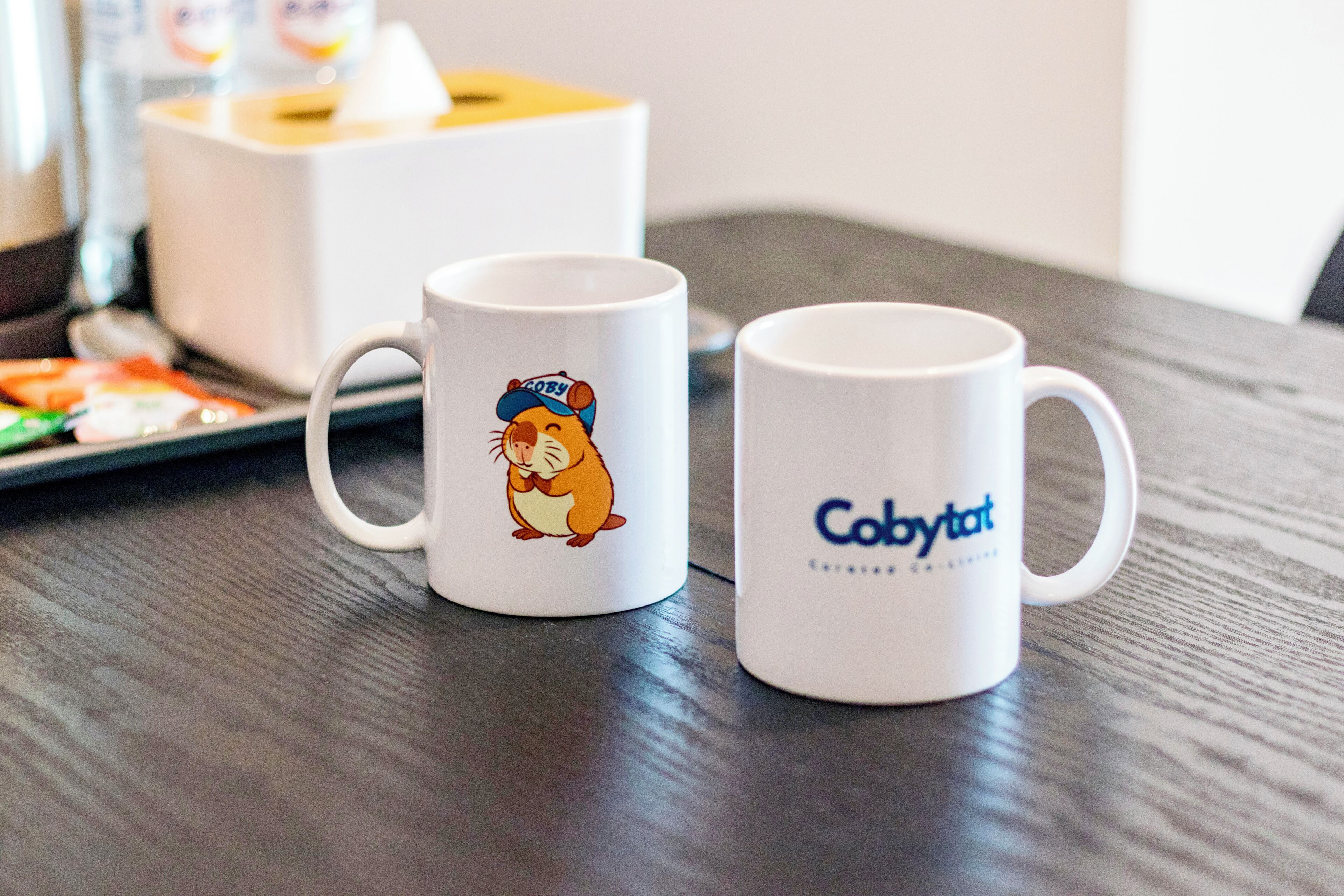 Two white mugs with a cartoon character and the text "Cobytat" on a wooden table.