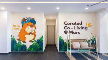 Un interior moderno con un personaje de caricatura en la pared, un sillón colgante y un letrero que indica Curated Co-Living at Marc.