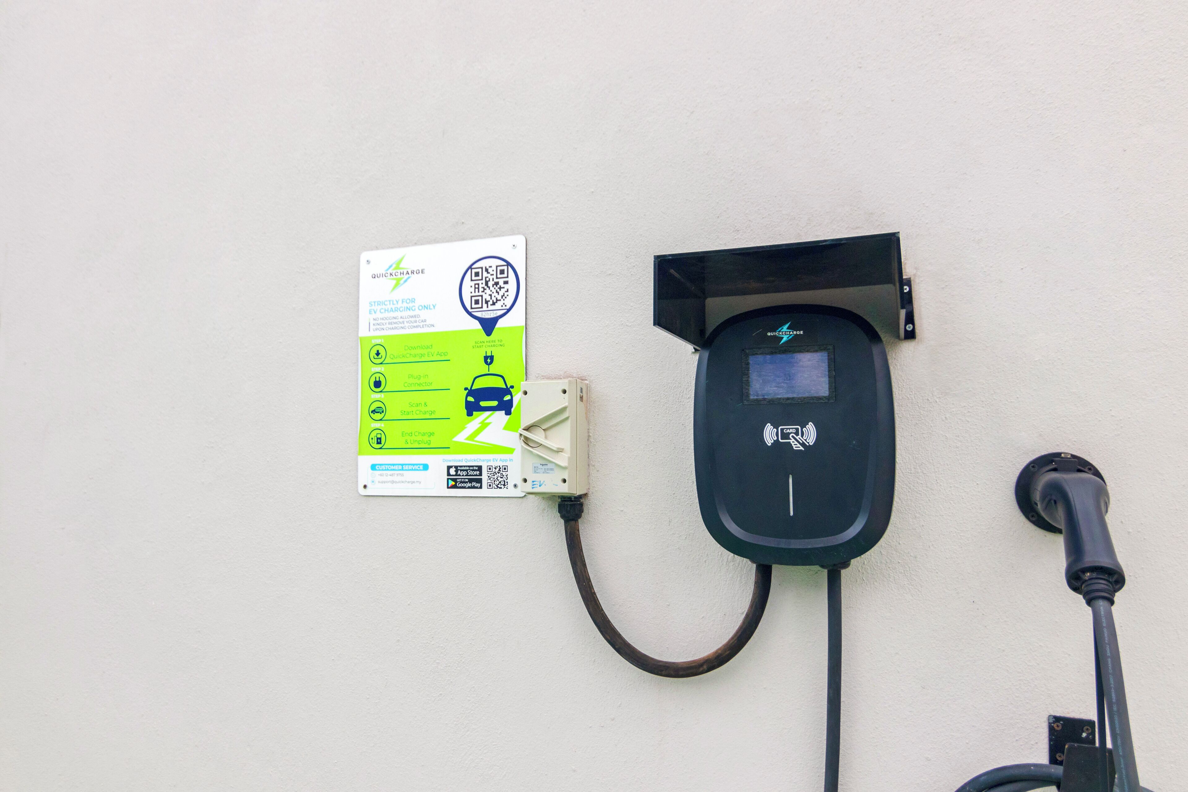 An electric vehicle charging station with a QR code and instructions on a sign.