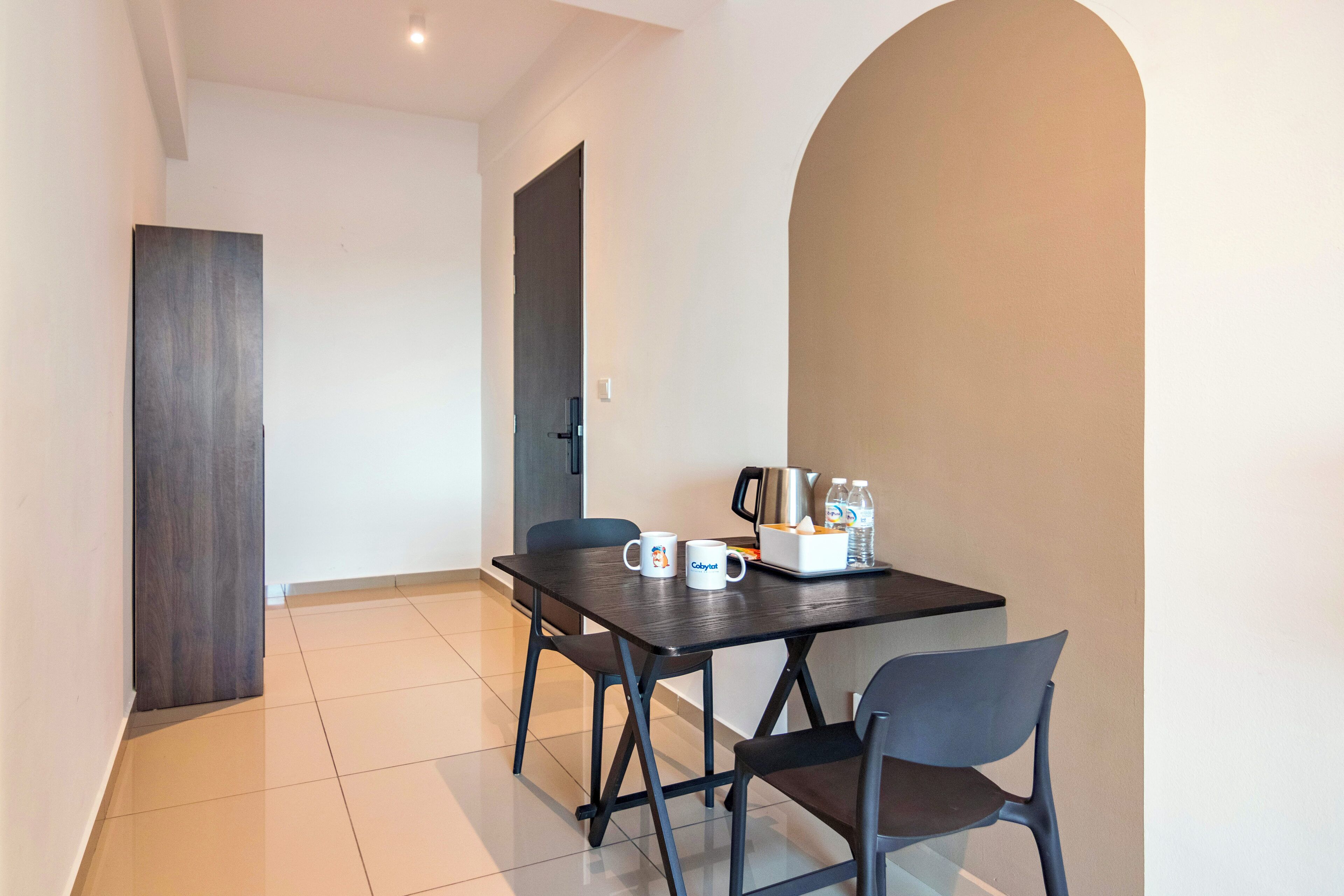 A modern dining area with a dark wooden table, two chairs, and a tray with a coffee pot, water bottles, and a mug.