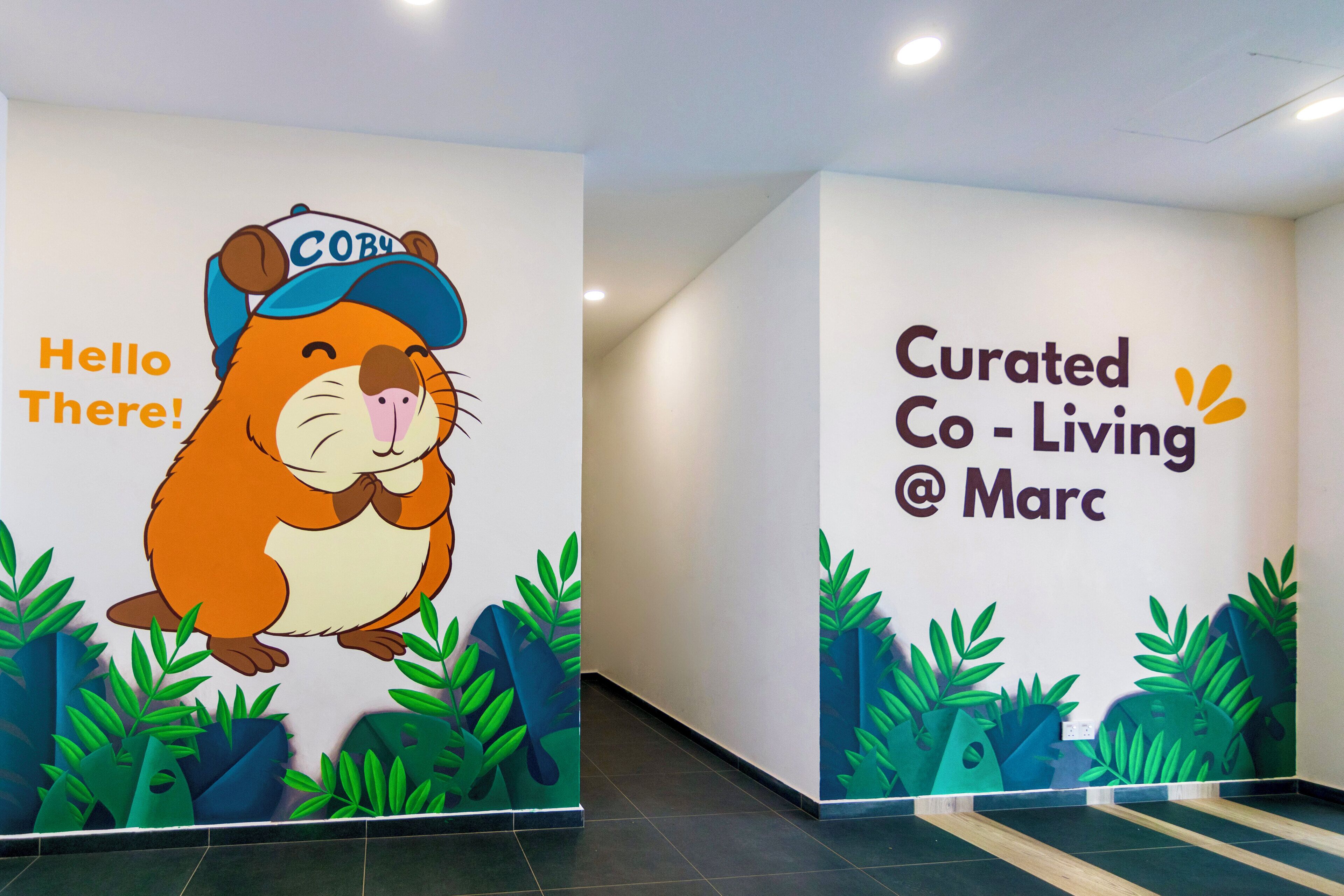 A hallway with a mural of a cartoon bear wearing a cap and the text "Hello There!" and "Curated Co-Living @ Marc".