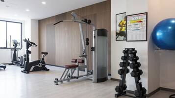 A modern gym with various exercise equipment, including an elliptical, a weight machine, and a set of dumbbells.